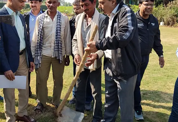 A group of people gathered outdoors as one man plants a sapling during a community tree-planting activity